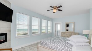 A bedroom with a bed, a ceiling fan, a TV mounted on the wall, and large windows with blinds. - THE OCEANFRONT GRAND RESORT: 17 BR Luxury with Unmatched Views+ALL THE AMENITIES (North Myrtle Beach)