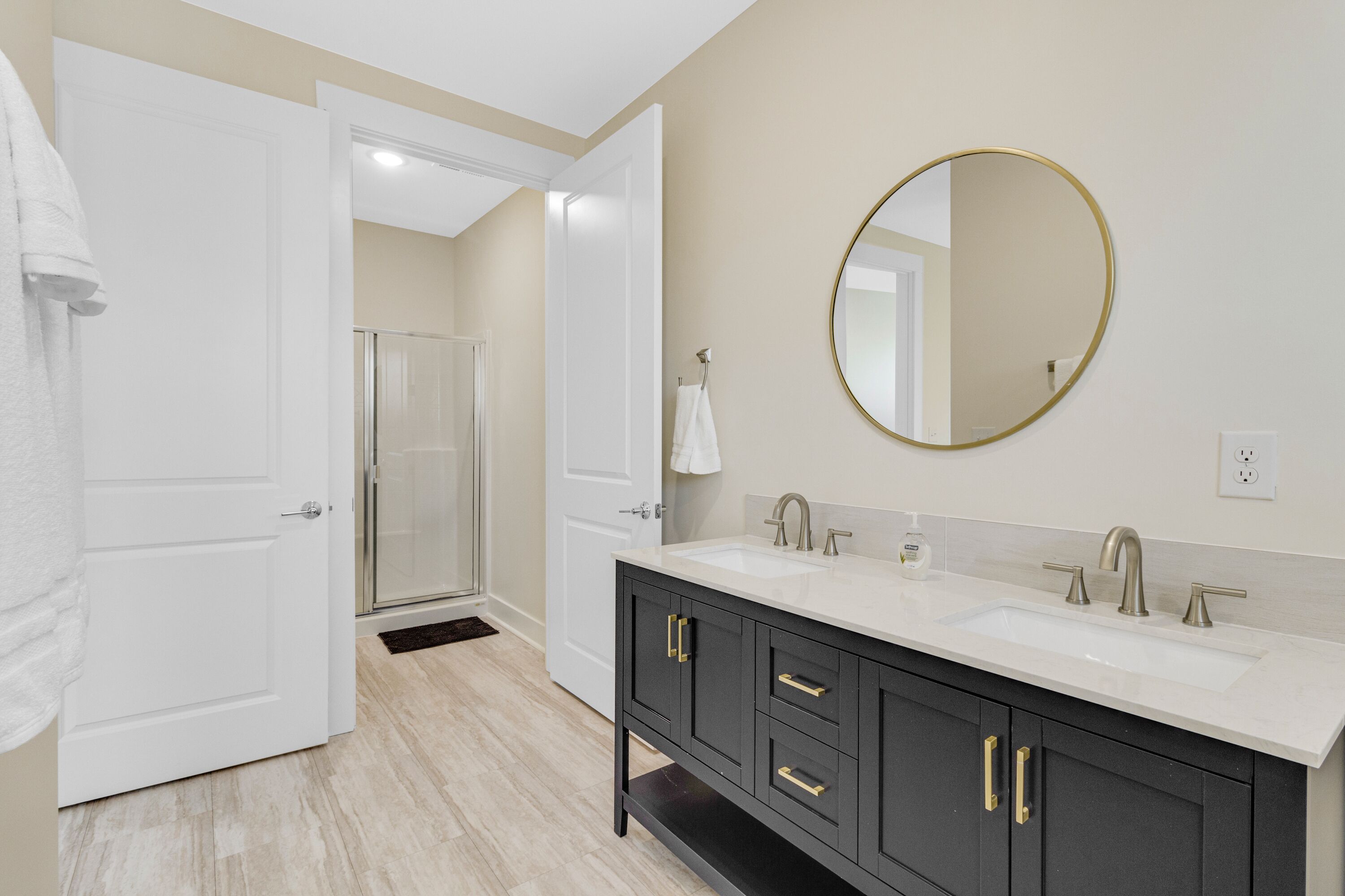 A modern bathroom with two sinks, a large mirror, and a walk-in shower.