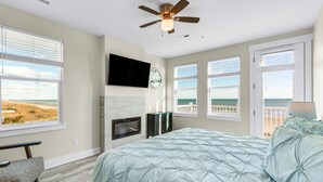 A bedroom with a large bed, a ceiling fan, a fireplace, a TV, and a view of the ocean. - Spectacular Oceanfront HOME Large Media&Game Room 12 bed 12 bath OVERSIZED POOL (North Myrtle Beach)