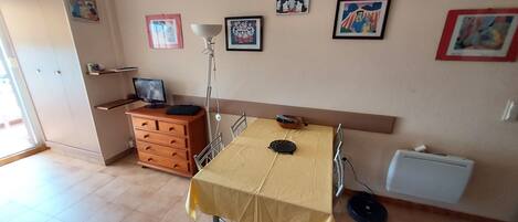 A dining area with a table, chairs, a television, a cabinet, and artwork on the wall.