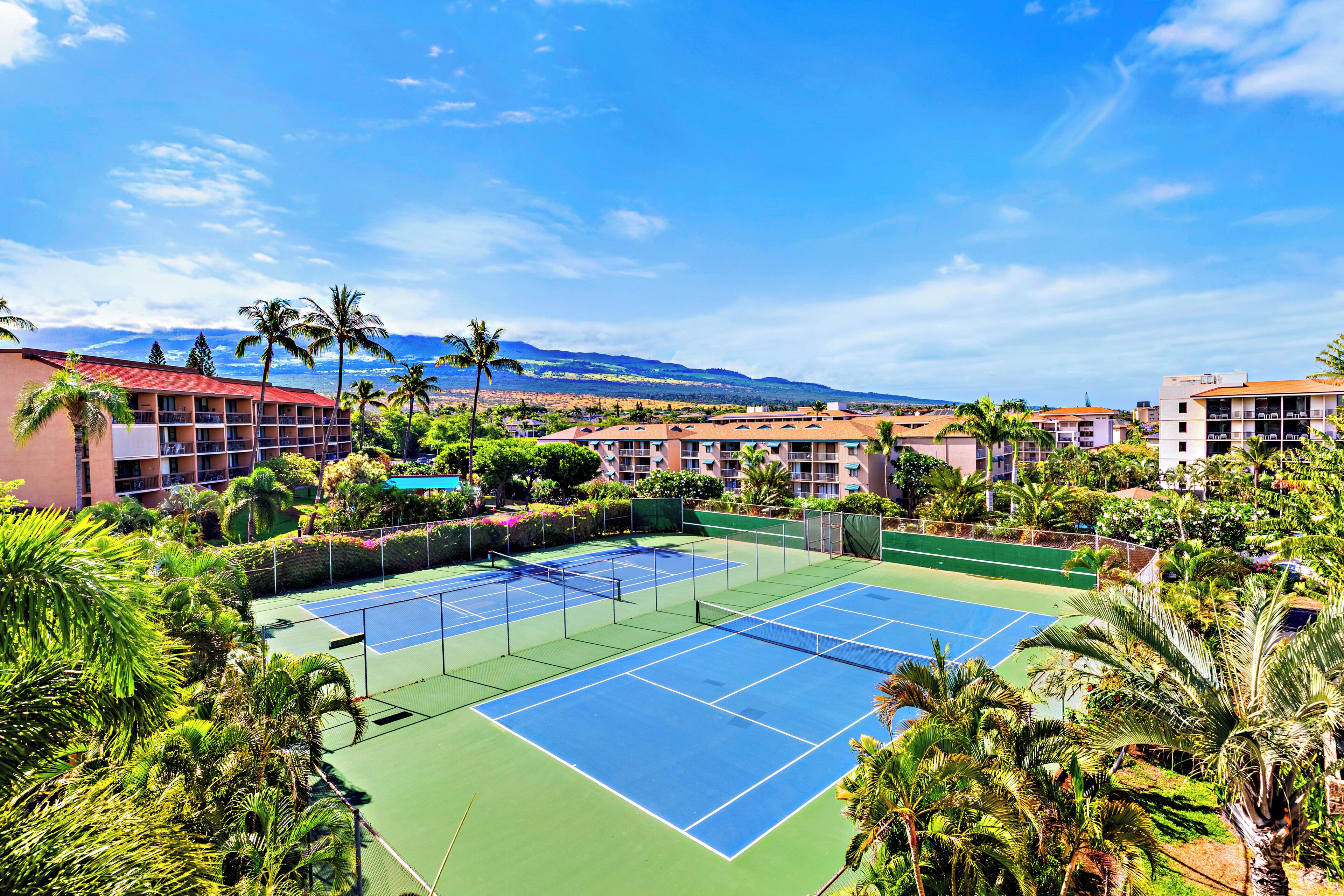 Ein Tennisplatz, umgeben von üppiger Vegetation und Hotelgebäuden.