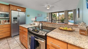 A modern kitchen with granite countertops, stainless steel appliances, and wooden cabinets. - Beach theme, private Lanai, pools and tennis courts (Kihei)