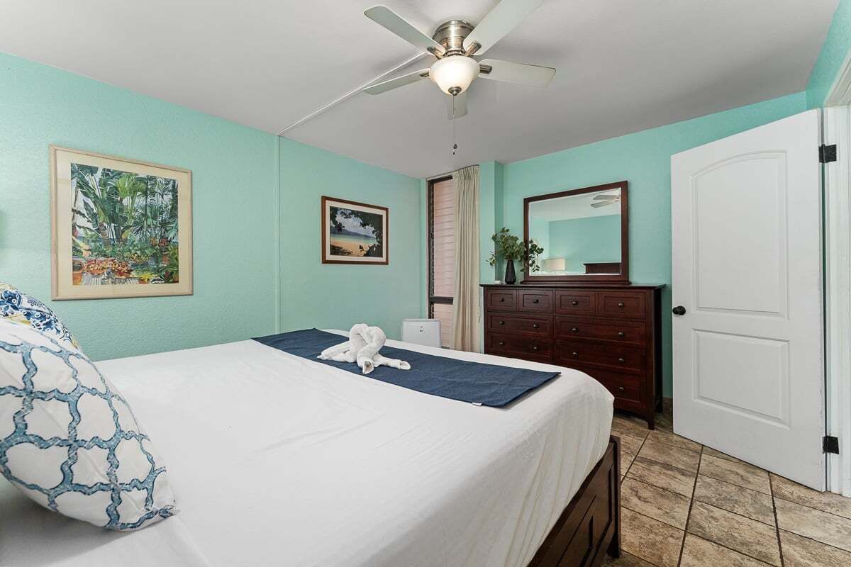Une chambre à coucher avec un lit, un ventilateur de plafond, une commode et une porte.