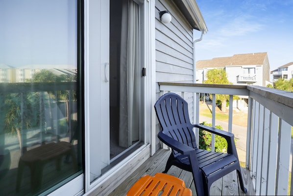 Une terrasse en bois avec une porte-fenêtre coulissante, une chaise noire et une chaise orange.