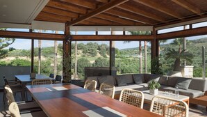 An open-plan living area with a wooden ceiling, large windows, a dining table, and a sofa. - Kipo paradiso villa, pool,spa,massage,yoga,gym (Kyrianna)