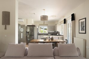 A modern kitchen with a dining area, a sofa with cushions, and a hanging light fixture.