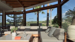 A modern interior with a sofa, a table, and a large window offering a view of palm trees and greenery. - Kipo paradiso villa, pool,spa,massage,yoga,gym (Kyrianna)