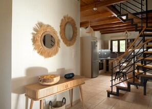 A kitchen with a wooden table, two wall-mounted mirrors, a refrigerator, and a staircase with wooden steps.