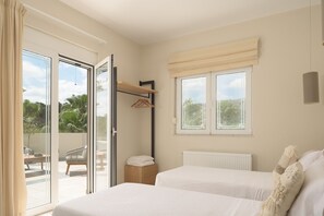 A hotel room with two beds, a small table, a chair, a radiator, and a window with a view of greenery. - Kipo paradiso villa, pool,spa,massage,yoga,gym (Kyrianna)