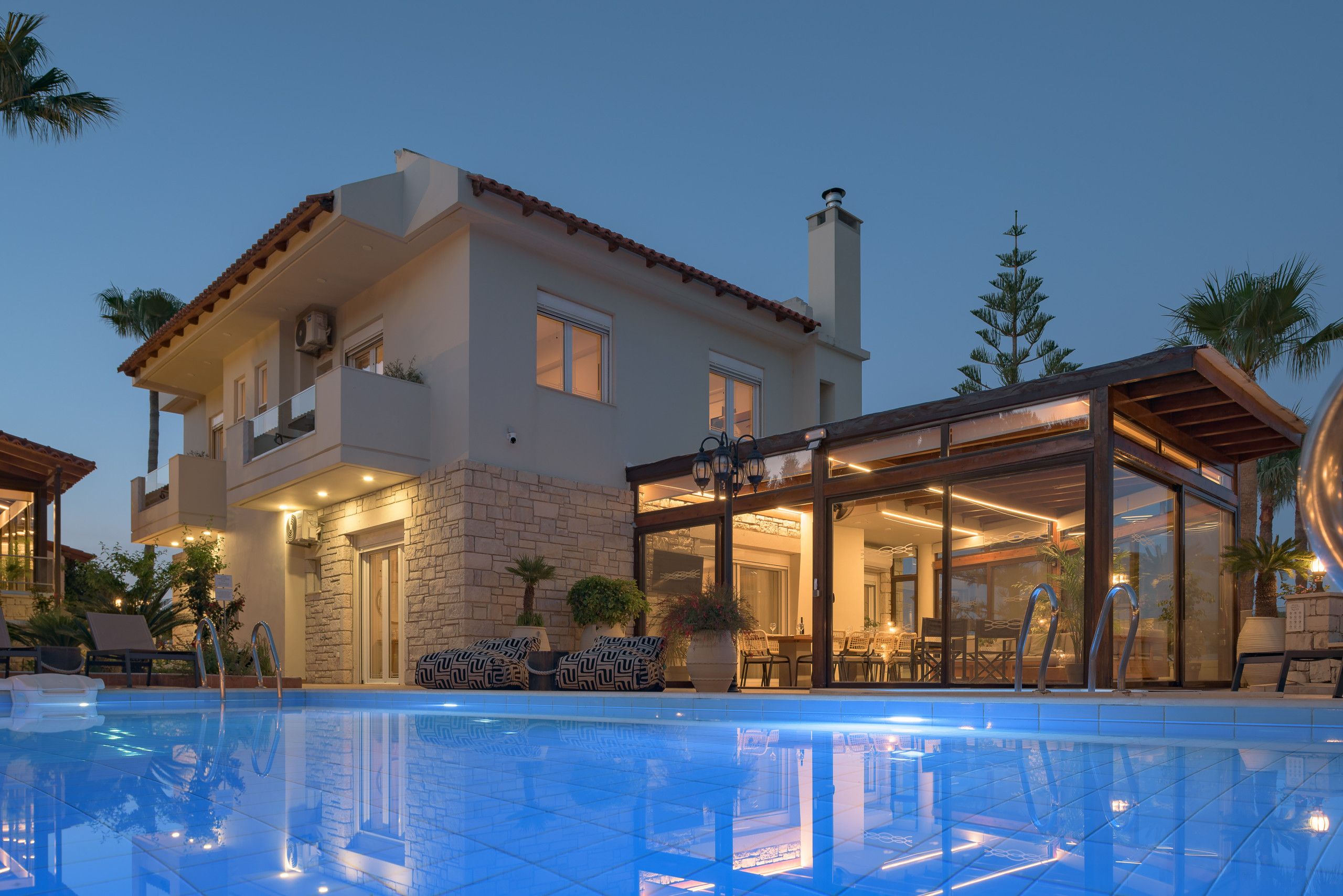 A modern house with a swimming pool, stone facade, and glass doors leading to an outdoor dining area.