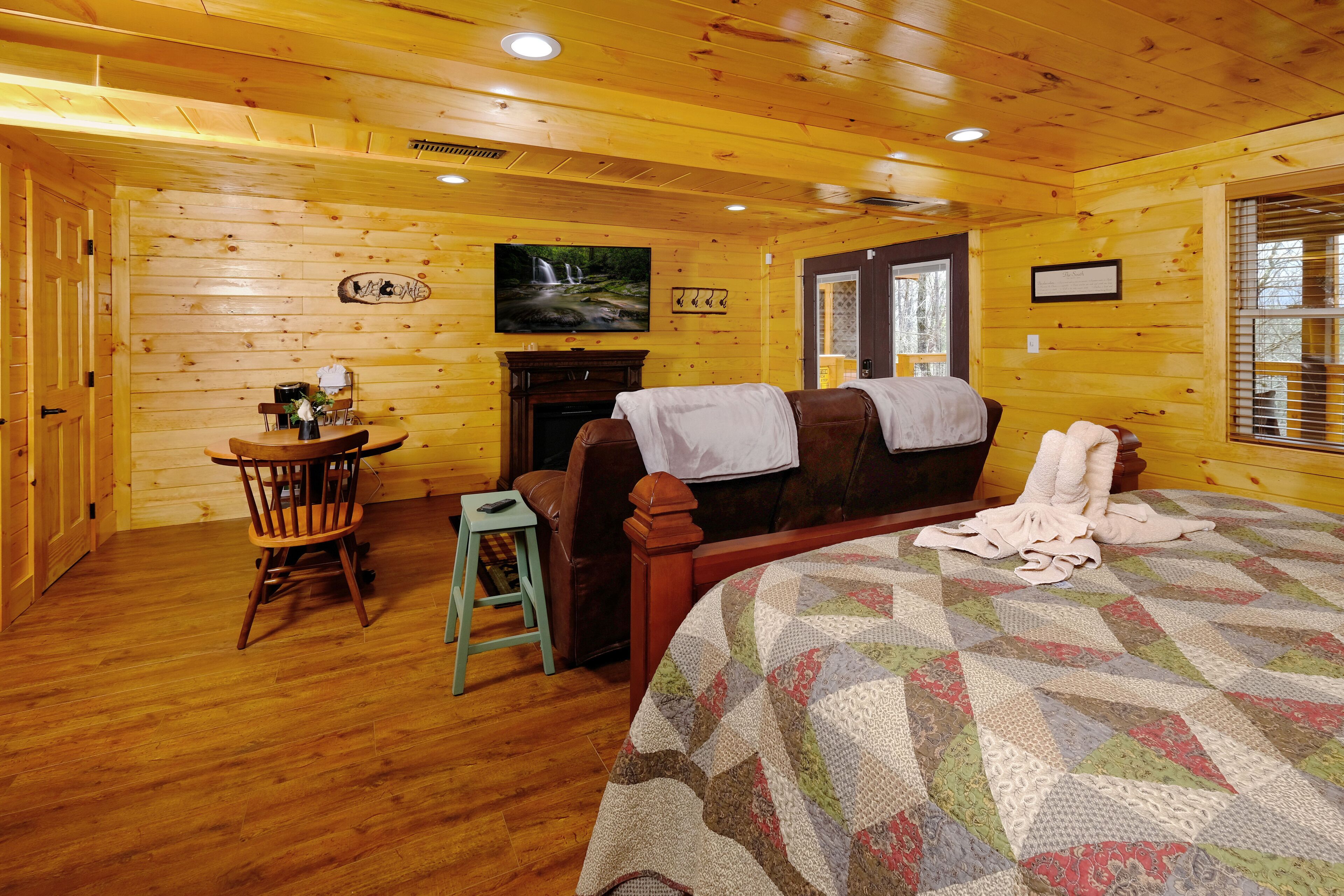 A wooden cabin room with a bed, a fireplace, a small table, and a chair.