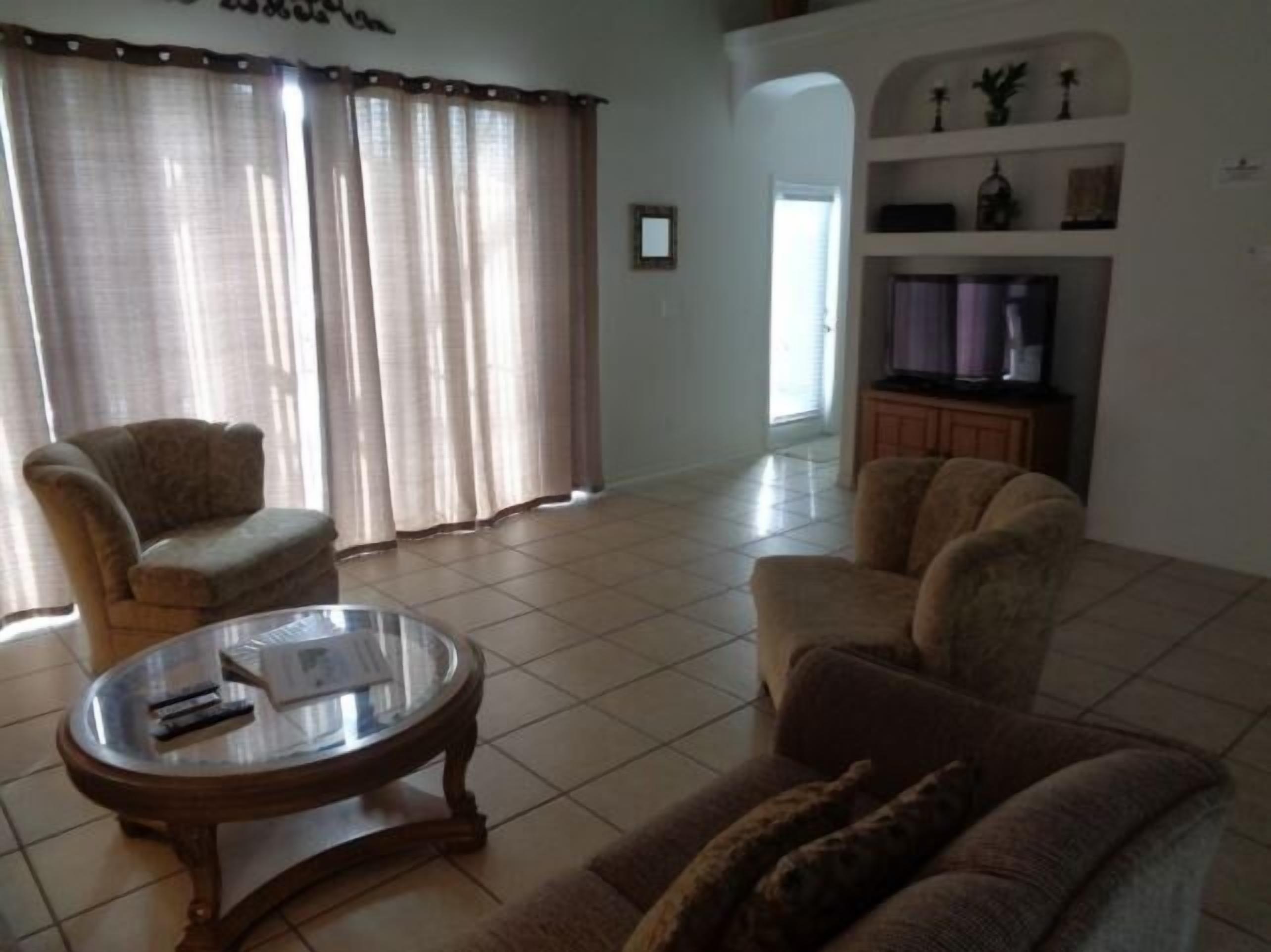 Uma sala de estar com sofá, poltronas, mesa de centro de vidro e televisão sobre um móvel.