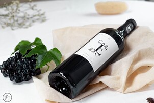 Una botella de vino etiquetada como "CAB ZINC" sobre una superficie blanca con un paño debajo.