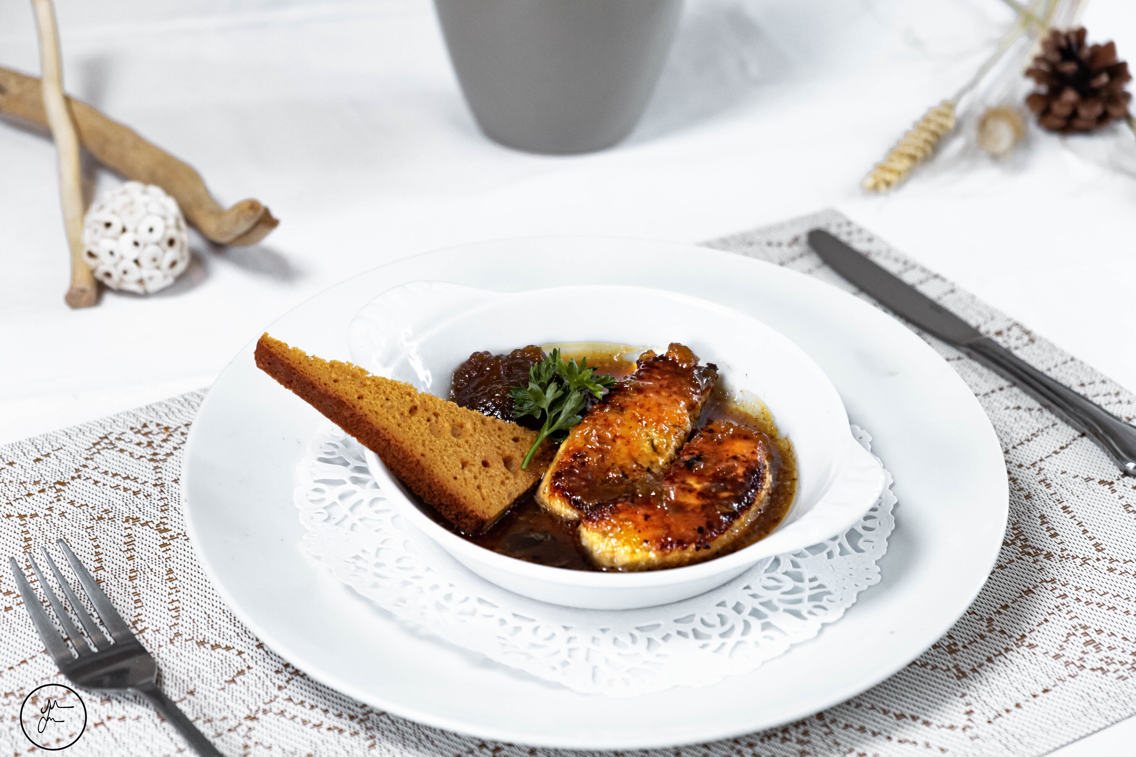 A white plate with a piece of meat, a slice of bread, and a garnish on a lace doily.