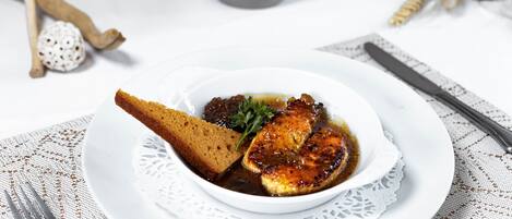 A white plate with a piece of meat, a slice of bread, and a garnish on a lace doily.