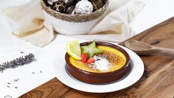 Un postre en un recipiente marrón sobre un plato blanco, decorado con lima, fresa y un elemento con forma de estrella, con una cuchara de madera al lado.