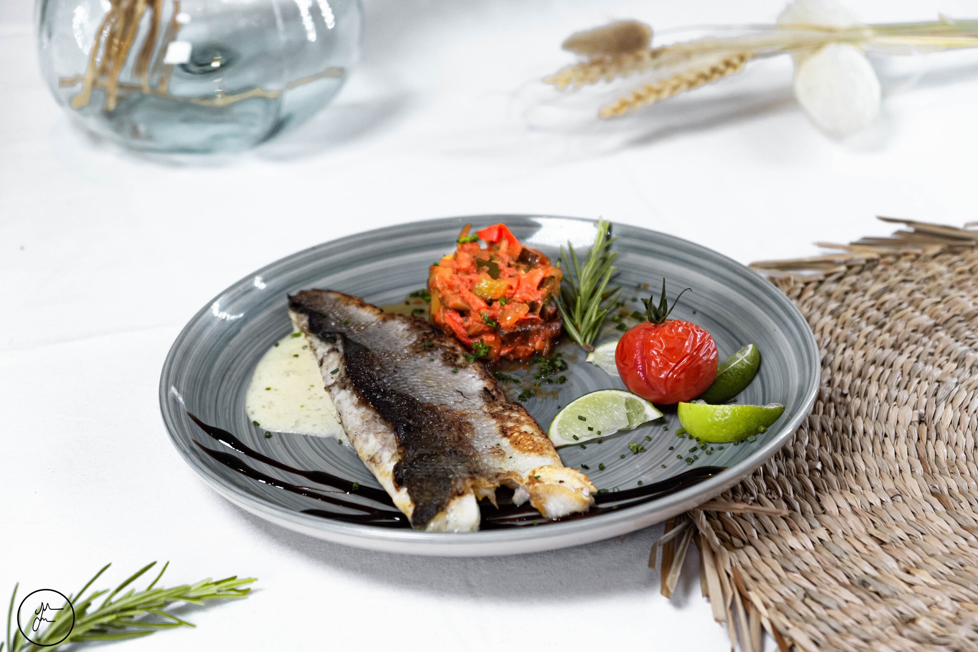 A plate with grilled fish, a tomato-based side, and lime wedges.