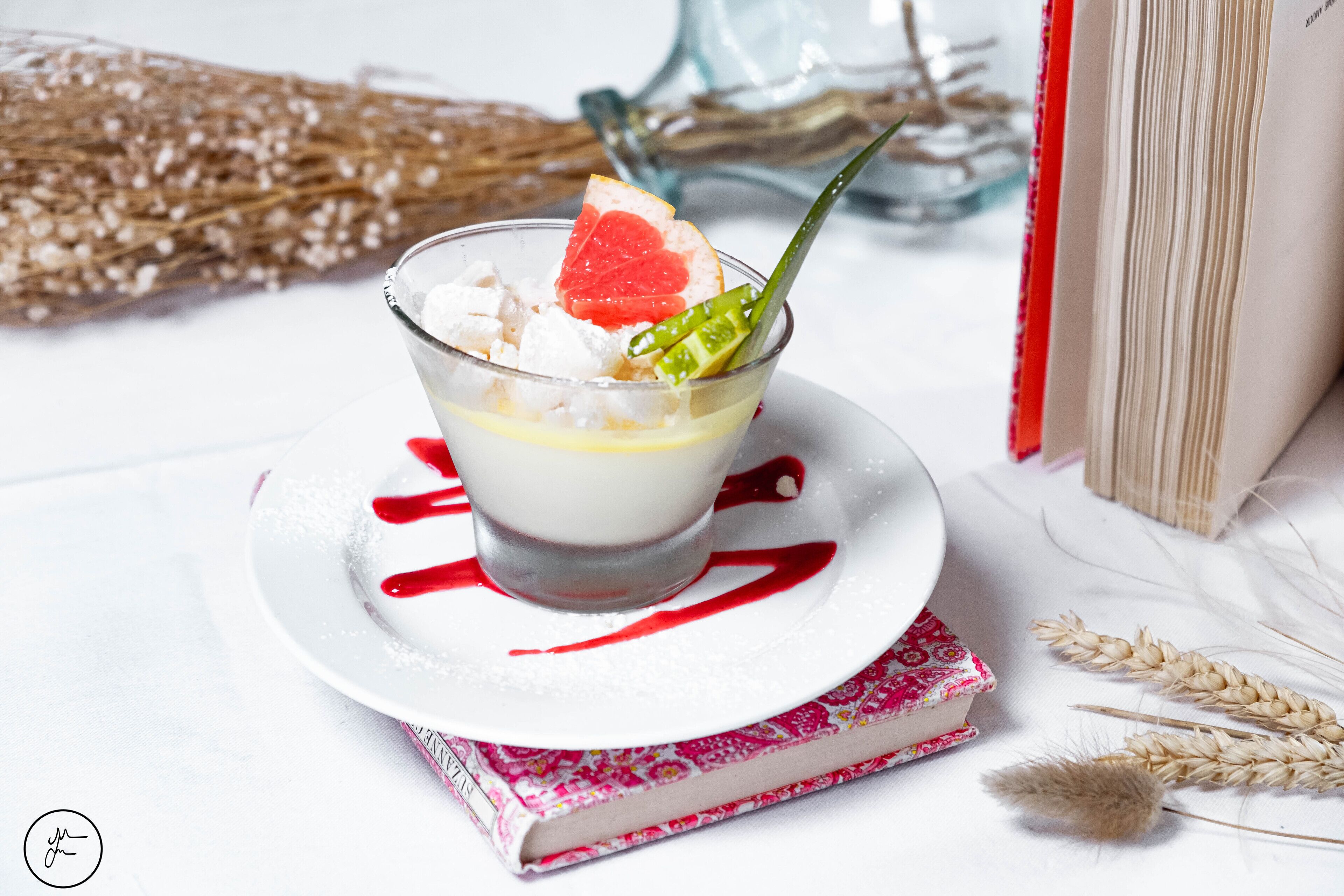 Een dessert met rode garnering, een boek en graanhalmen op een witte tafel.