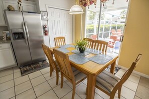Enjoy meals in this dining area with a table for four, a potted plant, and a kitchen with a refrigerator and oven.