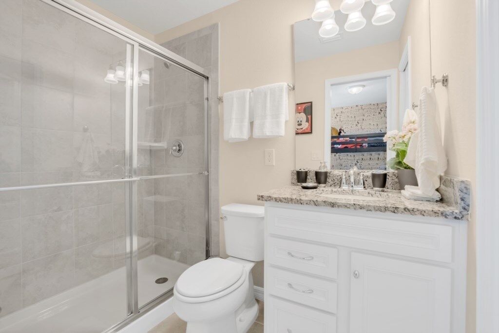 Un baño moderno con ducha envuelta en vidrio, inodoro blanco, tocador con encimera de mármol y un espejo grande.