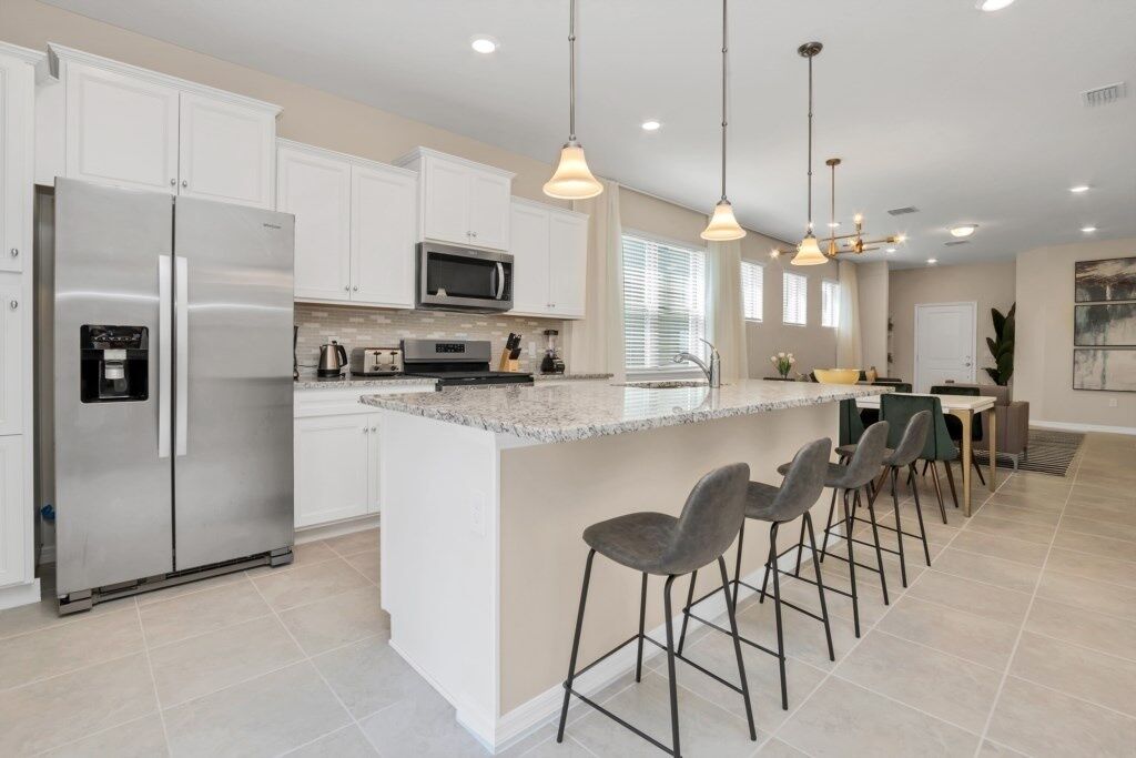 A modern kitchen with white cabinets, stainless steel appliances, a granite countertop, and bar stools.