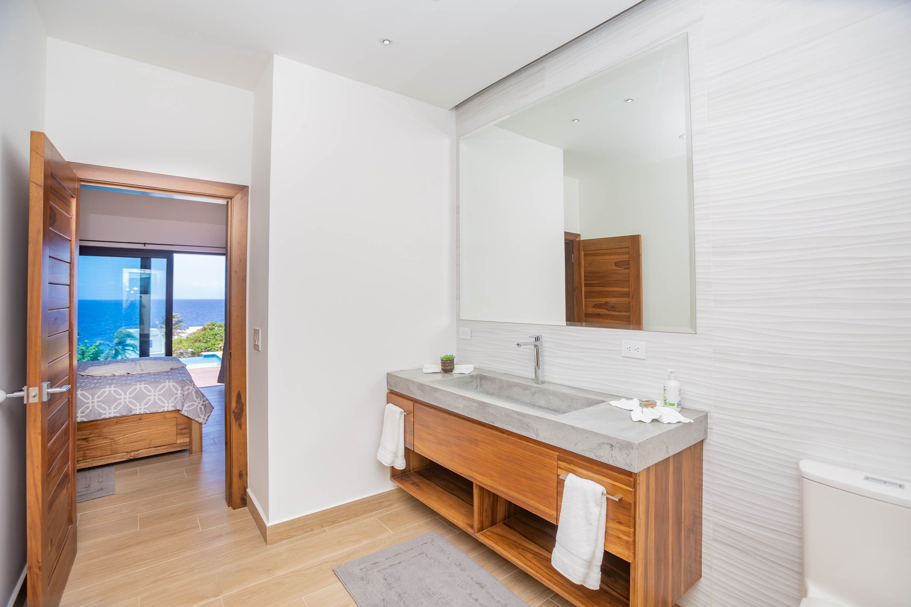 Ein modernes Badezimmer mit großem Spiegel, Holzwaschbecken und Meerblick.