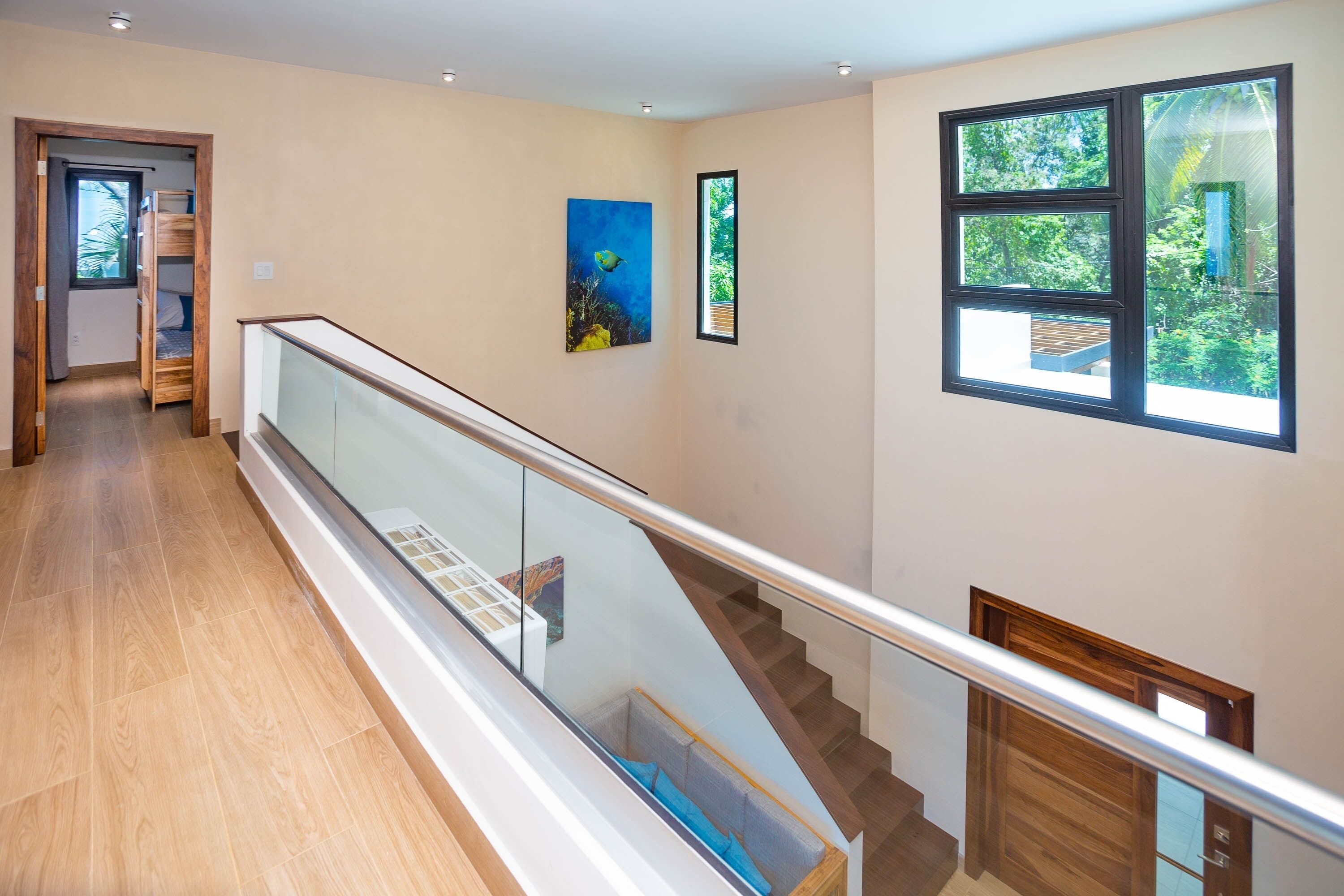 Ein modernes Interieur mit einer Holztreppe, einem Glasgeländer und Blick ins Grüne.
