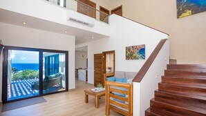 Amplia sala de estar con escalera de madera, balcón con vista al océano y comedor.