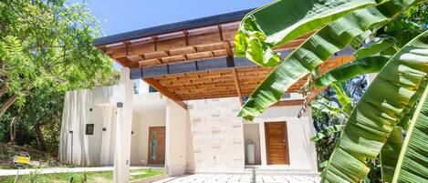 A modern building with a covered entrance, stone walls, and a paved area with a garden.