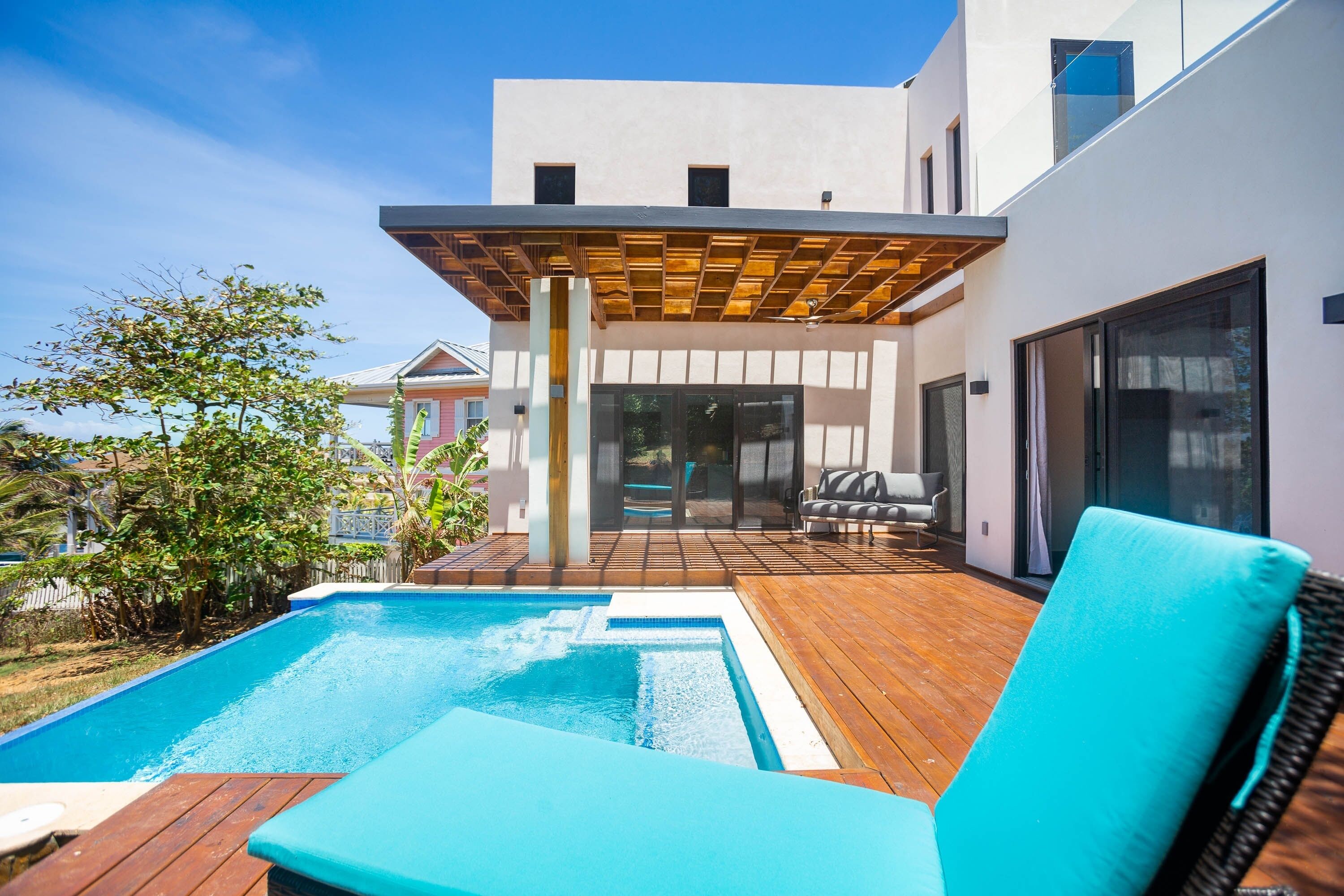 Zona de piscina exterior moderna amb terrassa de fusta i gandules.