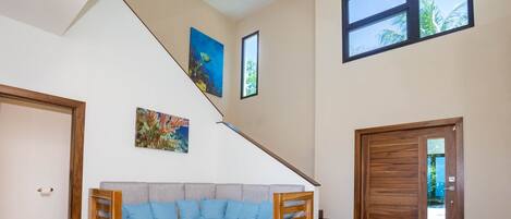 A modern living room with a grey sofa, wooden coffee table, and a staircase leading to a balcony.