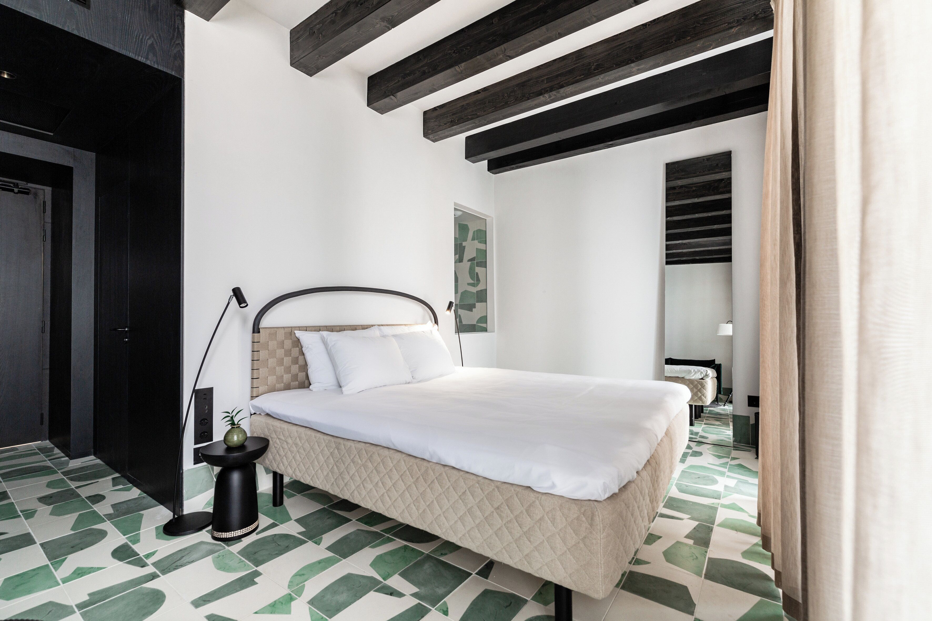 A modern bedroom with a bed, a small table with a plant, and a unique green and white patterned floor.
