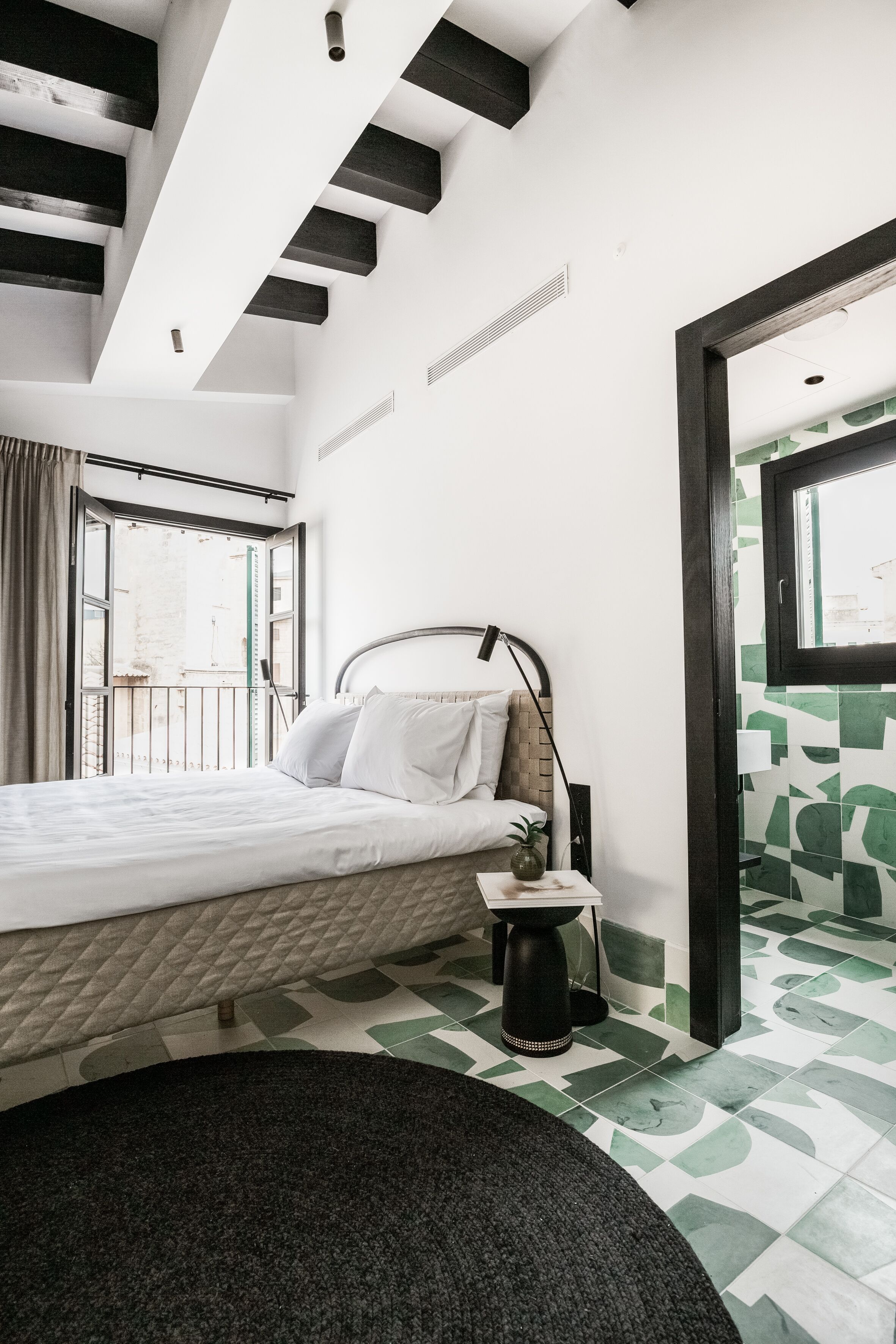 Une chambre à coucher avec un lit, une table de chevet, une lampe et une vue sur l’extérieur.