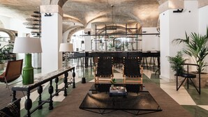 Un vestíbulo amplio con techos altos, una zona de bar central y diferentes disposiciones de asientos.