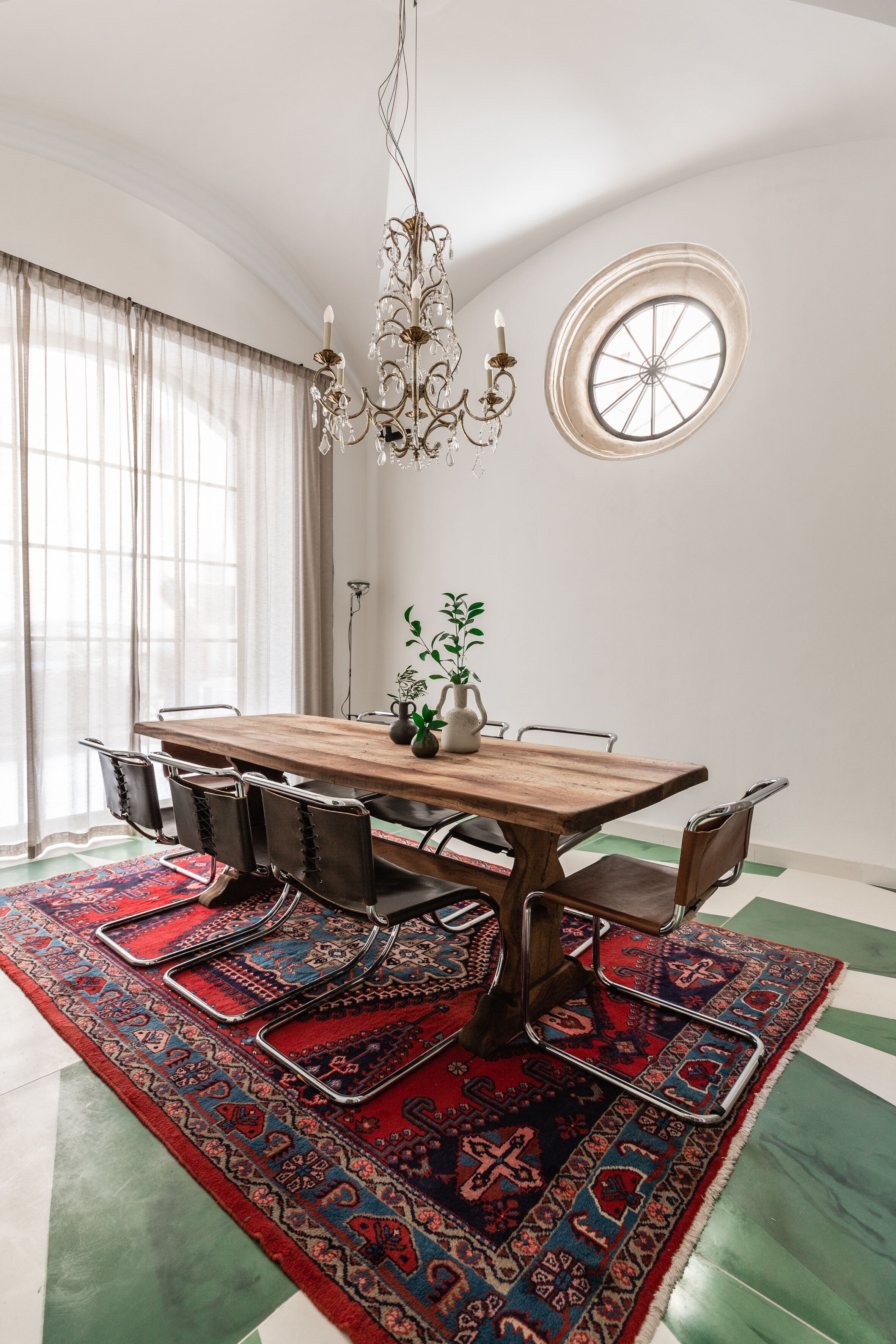 A dining area with a wooden table, chairs, a chandelier, and a patterned rug.