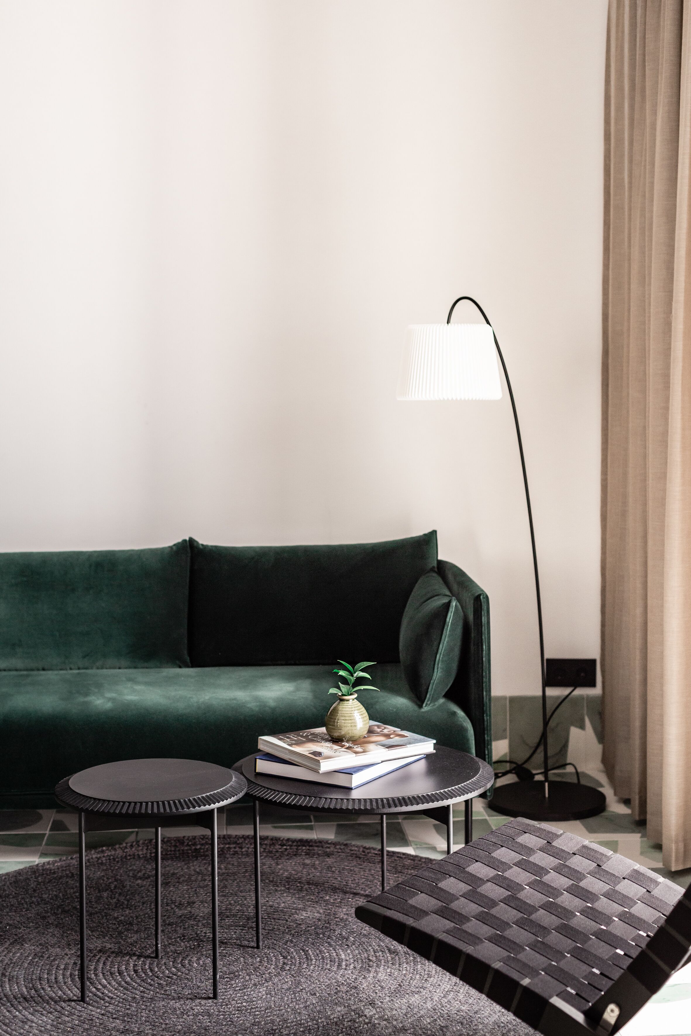 Una sala de estar moderna con un sofá verde oscuro, dos mesitas redondas, una lámpara de pie y una pequeña planta en maceta.