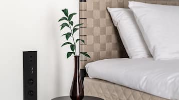 A modern bedroom with a bed, a bedside table with a vase, and a power outlet on the wall.