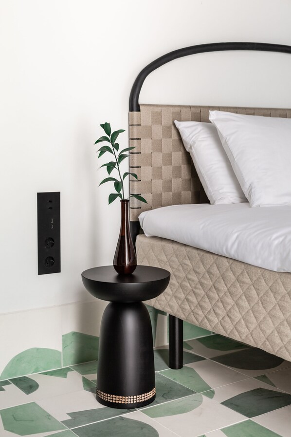 Un dormitorio moderno con una cama, una mesita de noche con un florero y un enchufe en la pared.