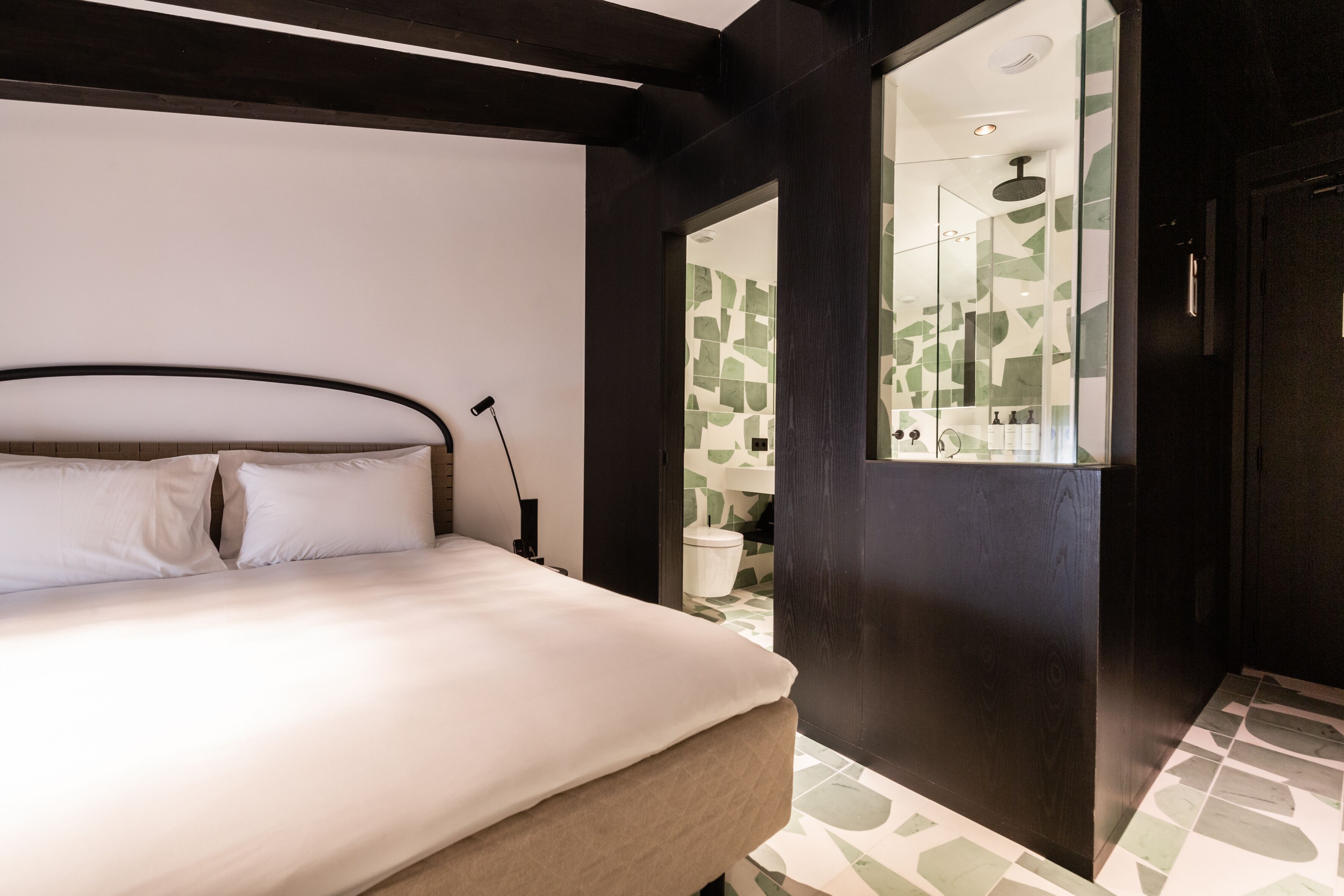 Ein modernes Hotelzimmer mit einem großen Bett, einem Nachttisch und einem durch eine offene Tür einsehbarer Badezimmer.
