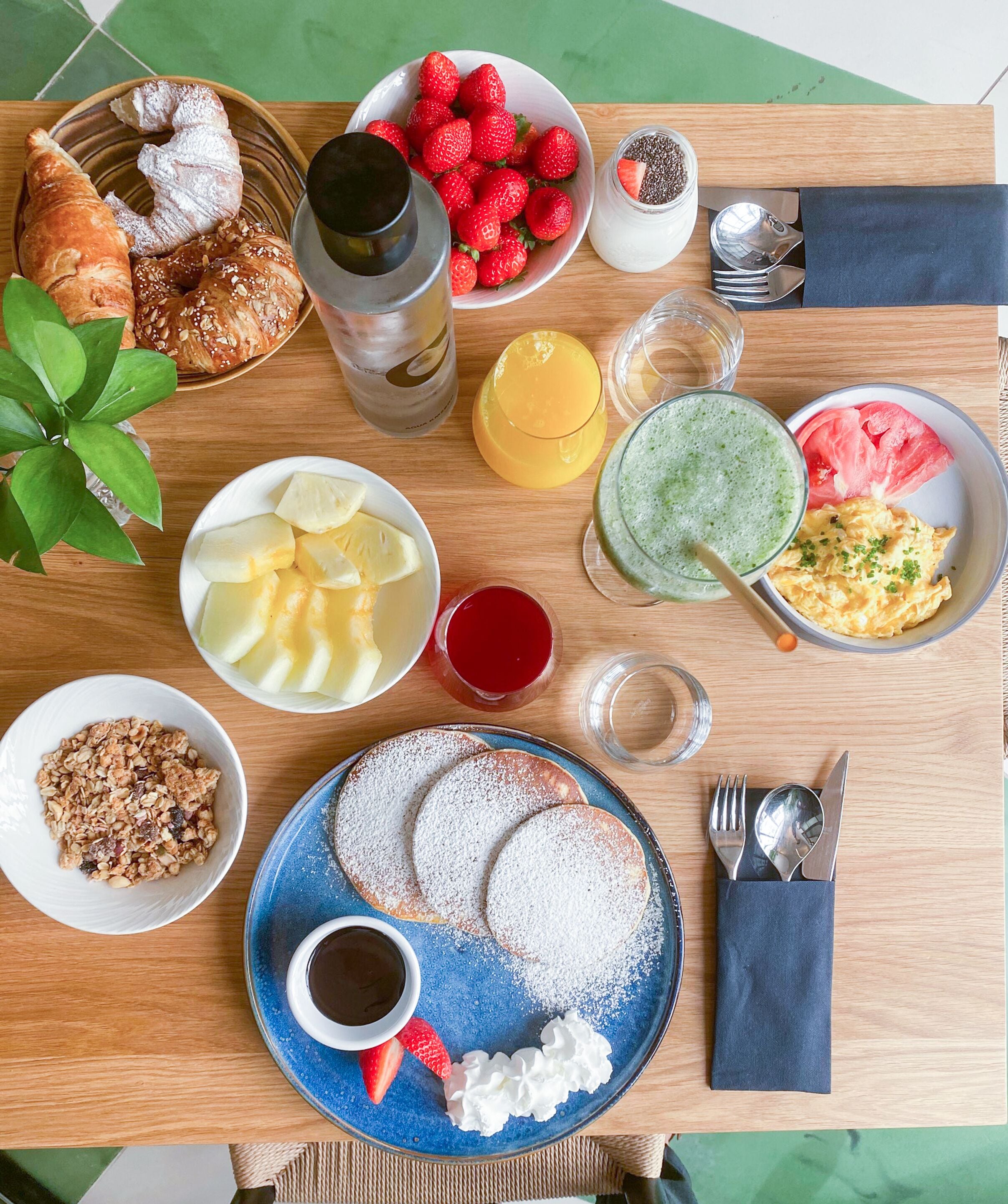 A breakfast table with croissants, strawberries, pancakes, and various beverages.