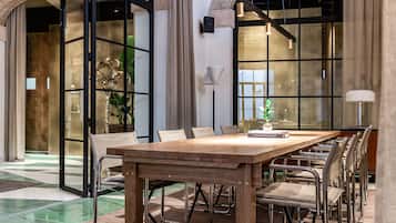 Een ruime eethoek met een lange houten tafel en metalen stoelen, omgeven door grote ramen en een gebogen stenen muur.