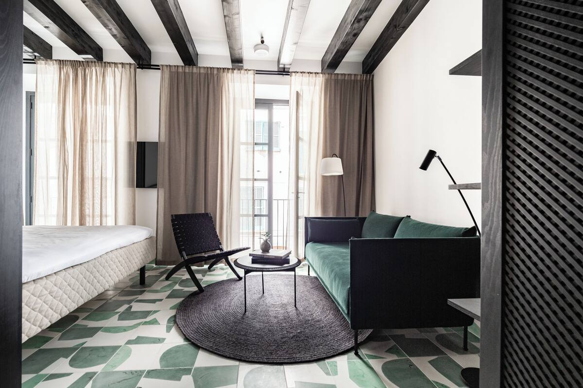 Ein modernes Hotelzimmer mit einem Bett, einer Couch, einem Sessel, einem kleinen Tisch und einer Lampe.