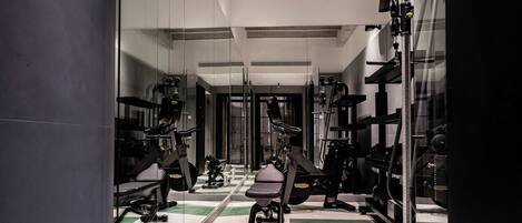 Une salle de sport avec des murs recouverts de miroirs, des appareils d’exercice et un sol à motifs en damier.
