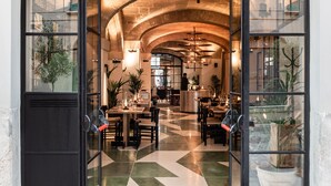 Un arco de entrada a un restaurante con suelo de cuadros, mesas, sillas y plantas en macetas.