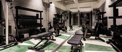 Un gimnasio con diversos equipos de ejercicio, paredes con espejos y un patrón de piso verde y blanco.