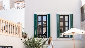 Una piscina con superficie de agua azul cristalina, una mujer con vestido blanco y un edificio blanco con contraventanas verdes.