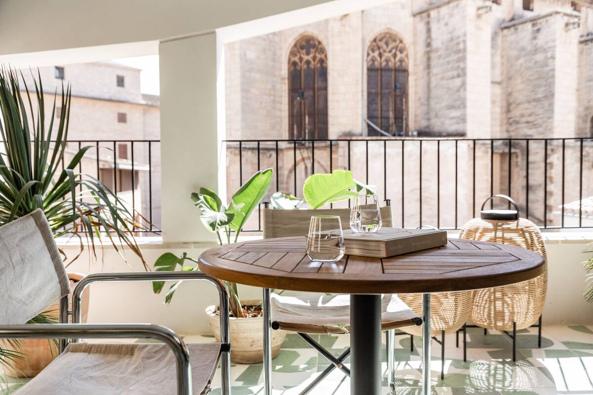 Ein Balkon mit rundem Tisch, Stühlen und Topfpflanzen.