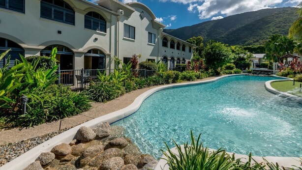 Un resort con piscina, rodeado de exuberante vegetación y montañas al fondo.