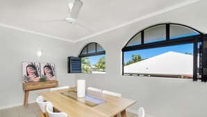 Un comedor moderno con una mesa de madera, sillas blancas y un ventilador de techo.