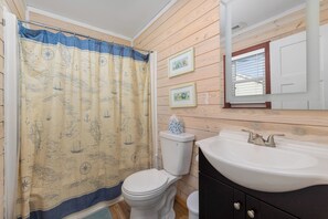 A bathroom with a nautical-themed shower curtain, a white toilet, a sink with a mirror, and wooden paneling on the walls. - Oceanviews- Walk to beach in 2 mins. Pets welcome  (Kitty Hawk)